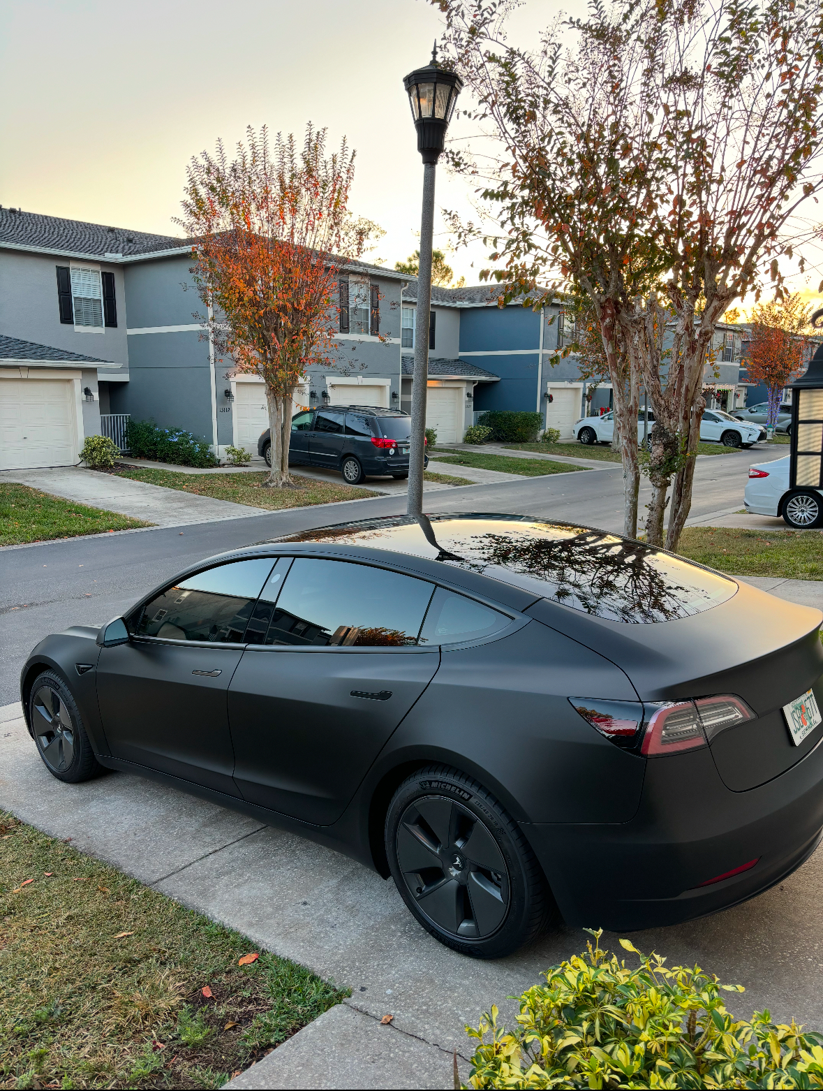 Matte black Tesla Model 3 rear three-quarter view with tinted glass roof and rear windows at sunset